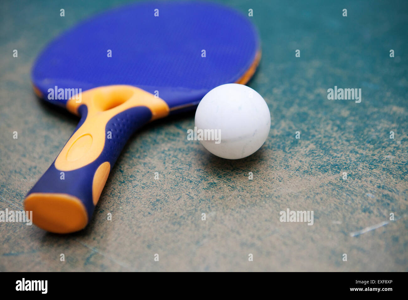 Table tennis paddle and ball on worn table Stock Photo