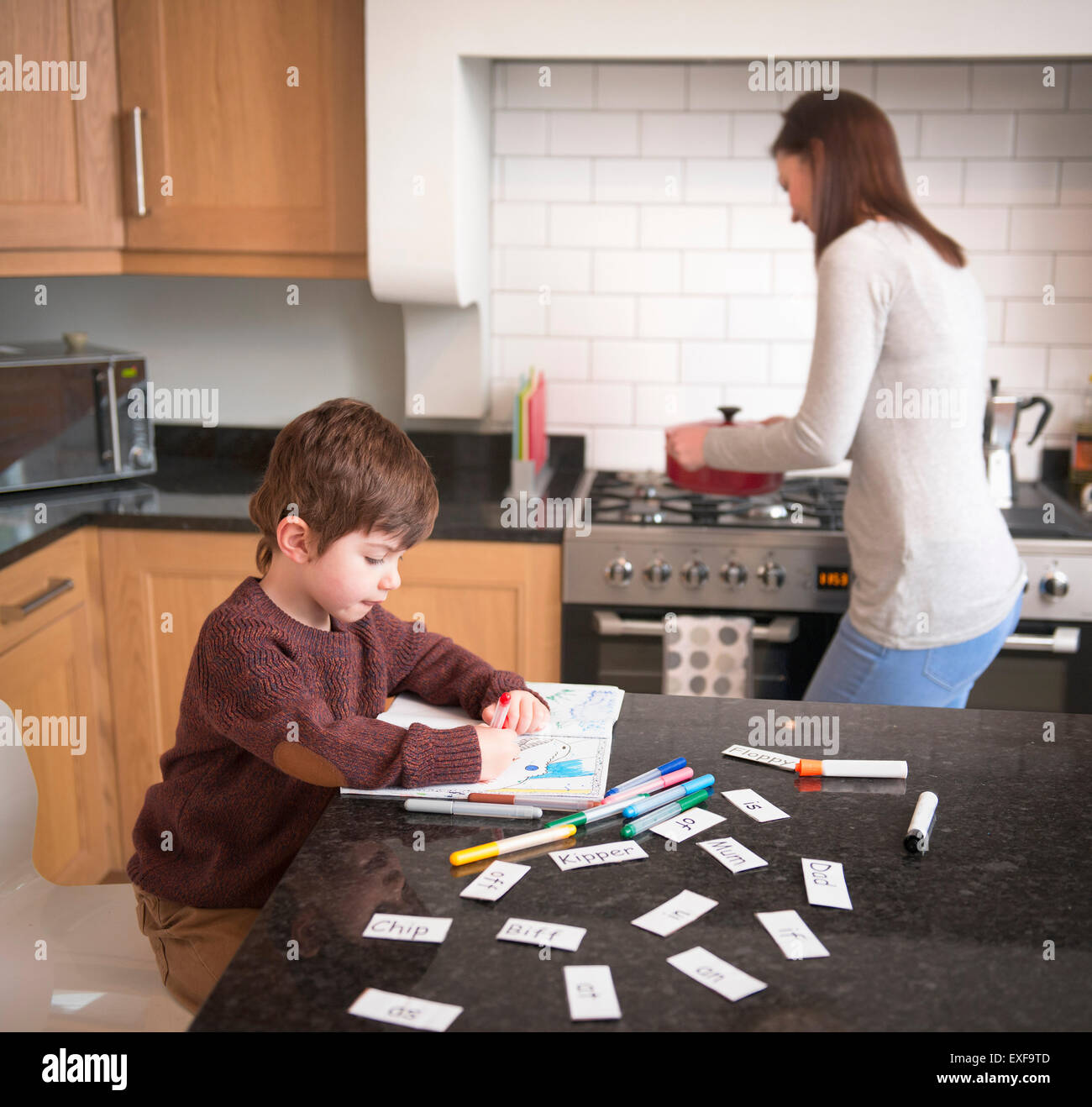 Boy coloring in book on kitchen counter as mother prepares dinner Stock Photo