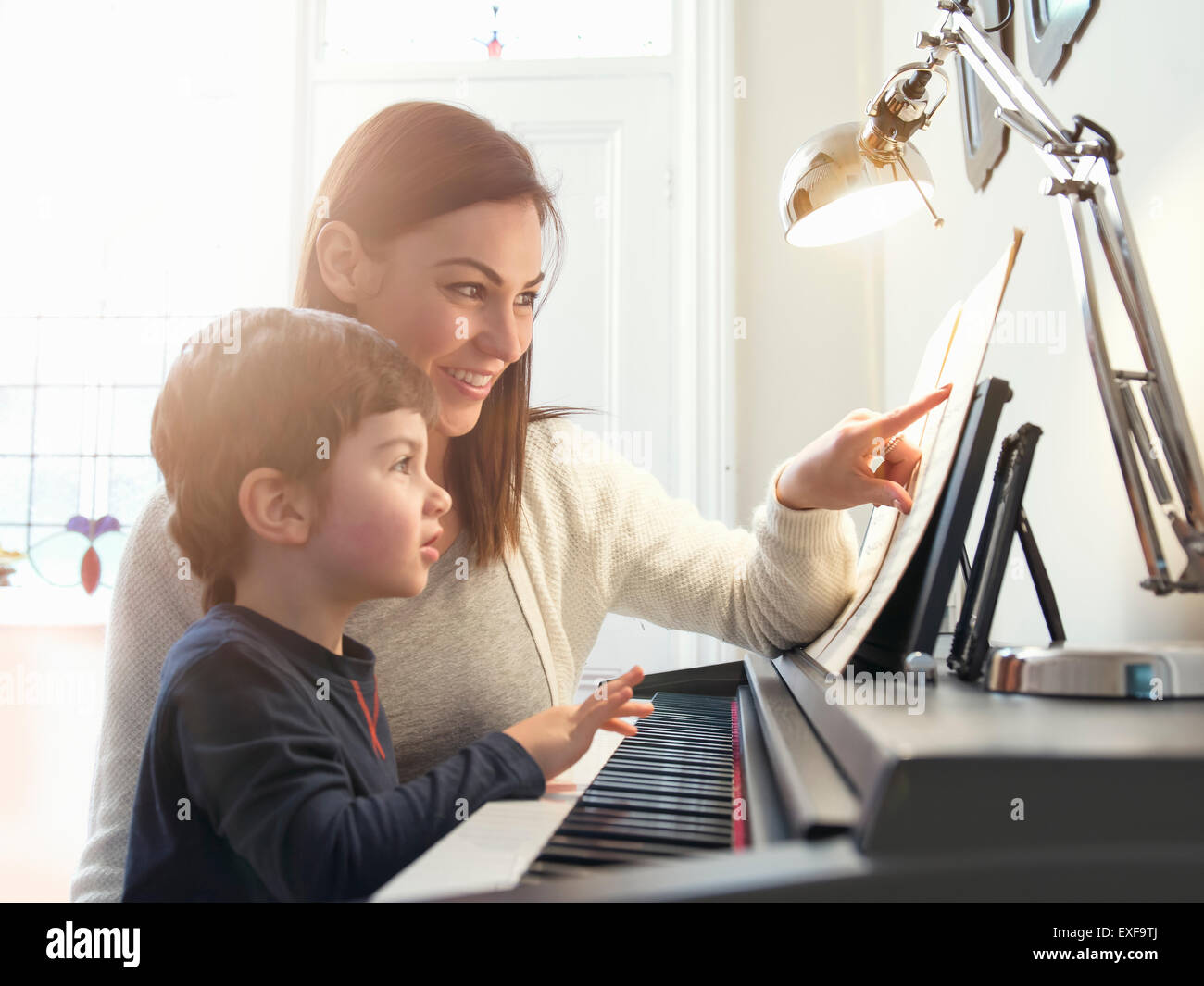 Mother pointing at sheet music to teach son to play piano at home Stock Photo