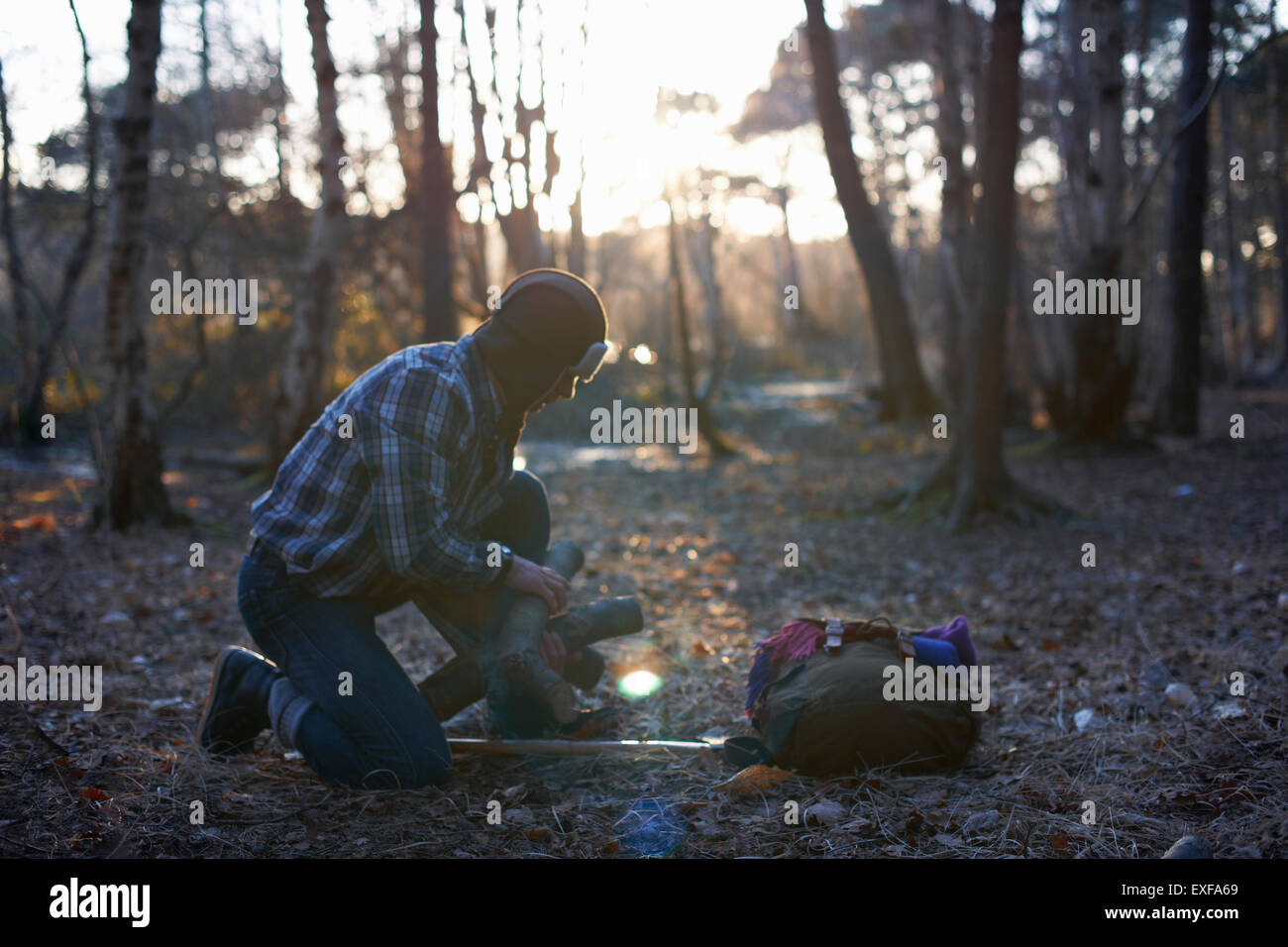 Mature male backpacker stacking logs for campfire in forest Stock Photo