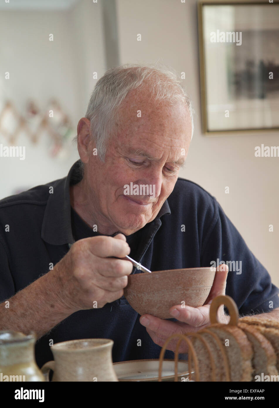 Senior man, sitting at table, eating bowl of cereal Stock Photo