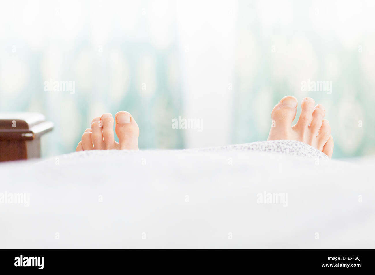 Pair of feet sticking out under duvet Stock Photo