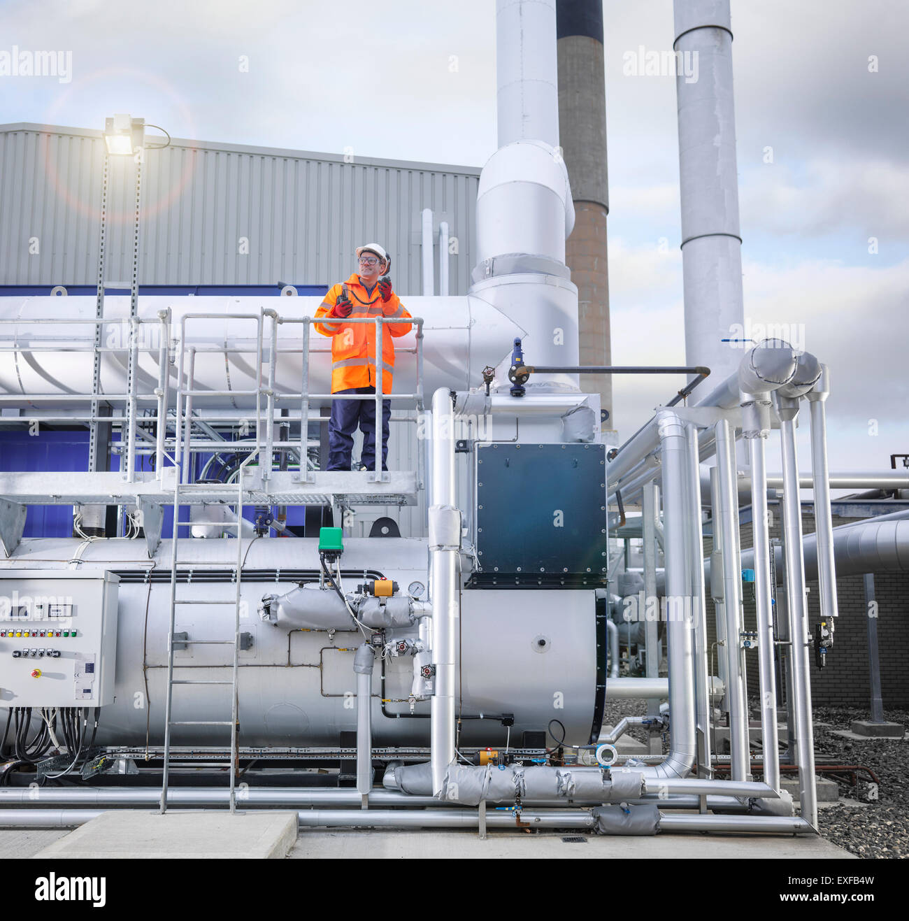 Worker standing amongst pipework of gas fired power station Stock Photo