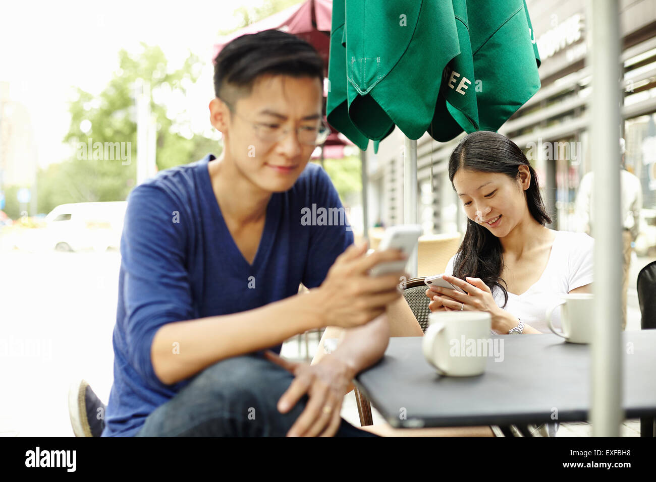 Tourist couple distracted by smartphones at sidewalk cafe, The Bund, Shanghai, China Stock Photo