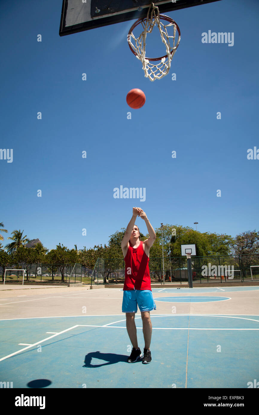 Young male basketball player throwing ball toward basketball hoop Stock
