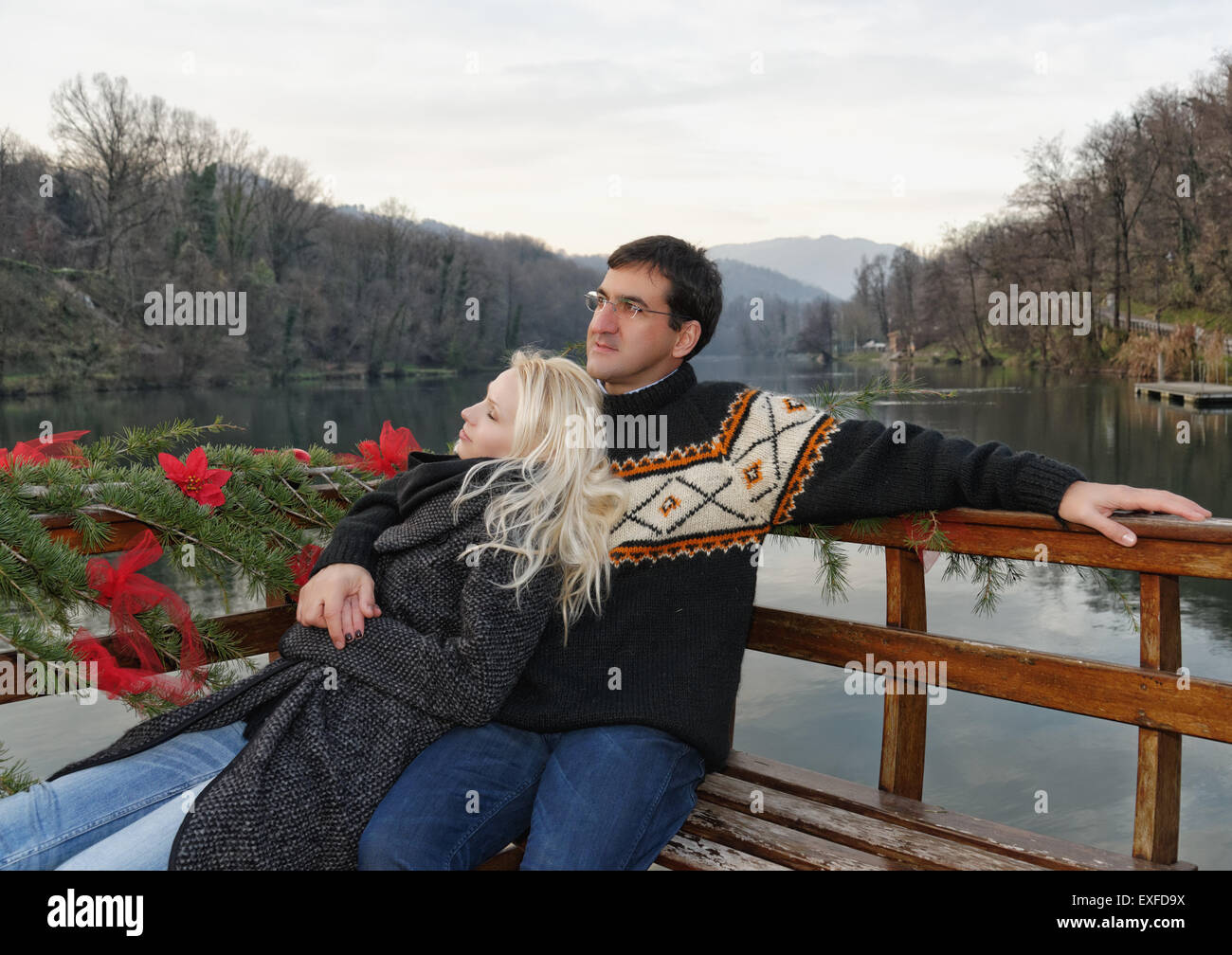 Heterosexual couple relaxing on bench beside lake, Lombardy, Italy Stock Photo