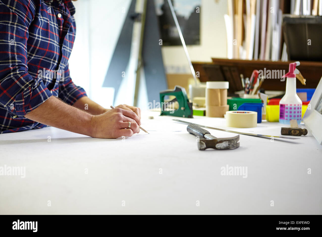 Mid adult man writing measurement on workbench in picture framers workshop Stock Photo