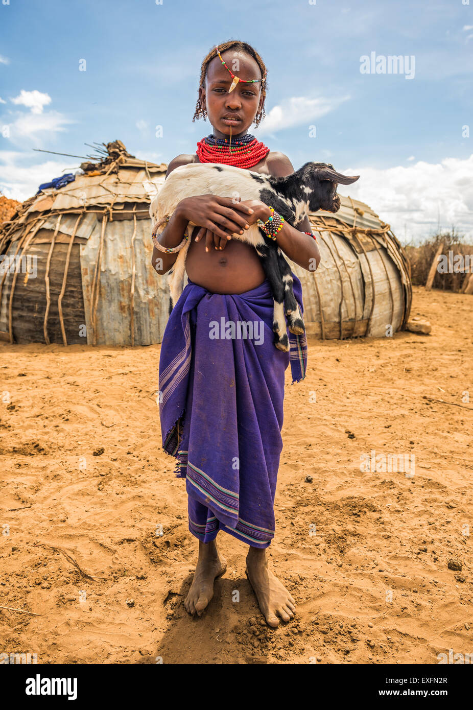 Girl from the African tribe Dasanesh holding a goat in her village Stock Photo