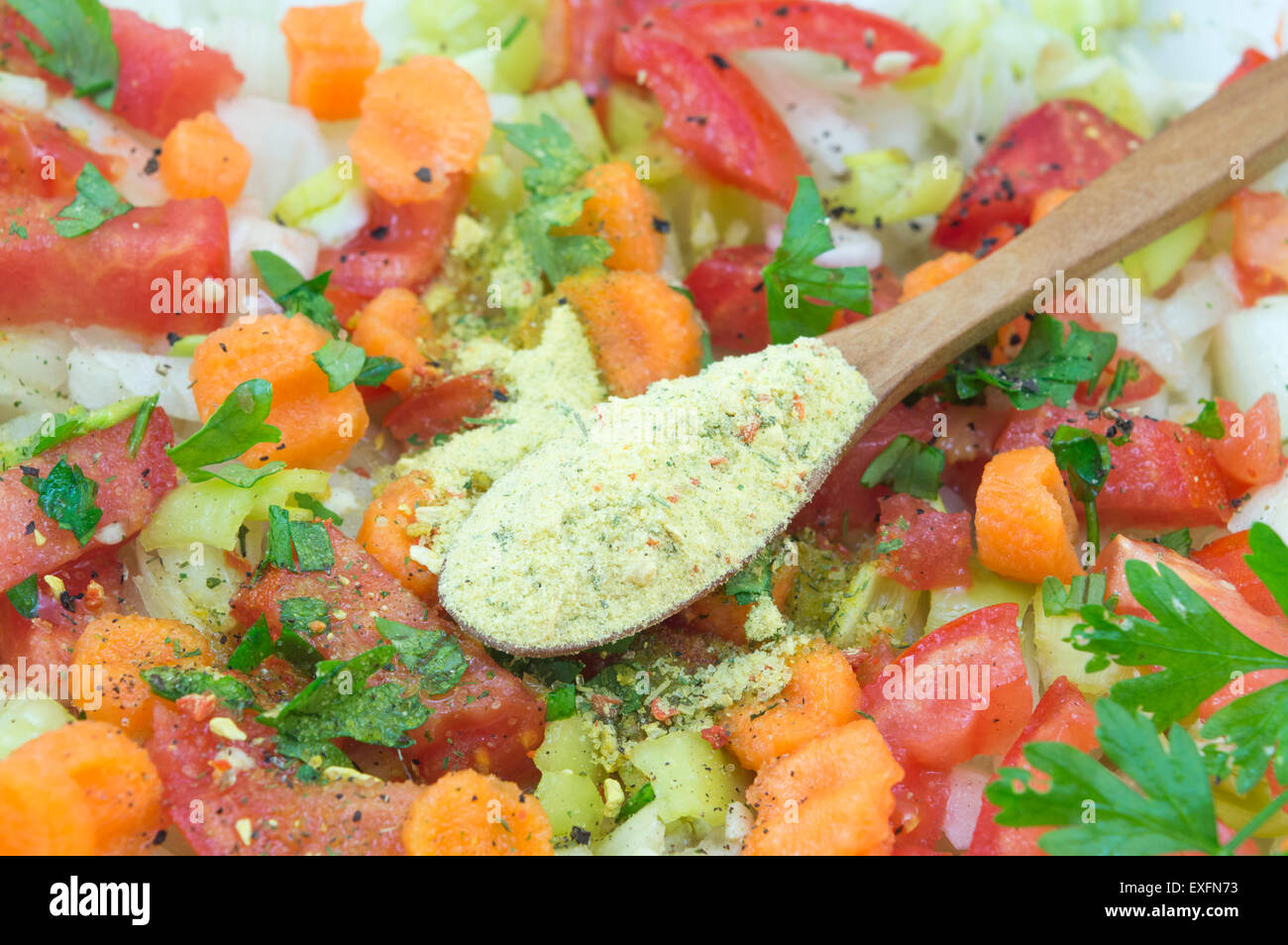 Seasoning in a wooden spoon on top of the vegetable salad with tomato,cucumber,parsley,carrot,paprika and onions Stock Photo