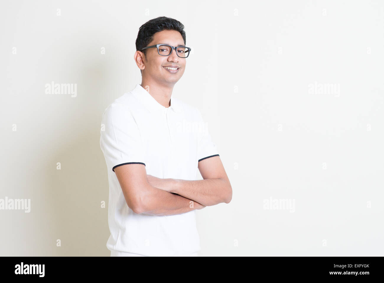 Portrait of happy Indian guy arms crossed looking at camera. Asian man standing on plain background with shadow and copy space. Stock Photo
