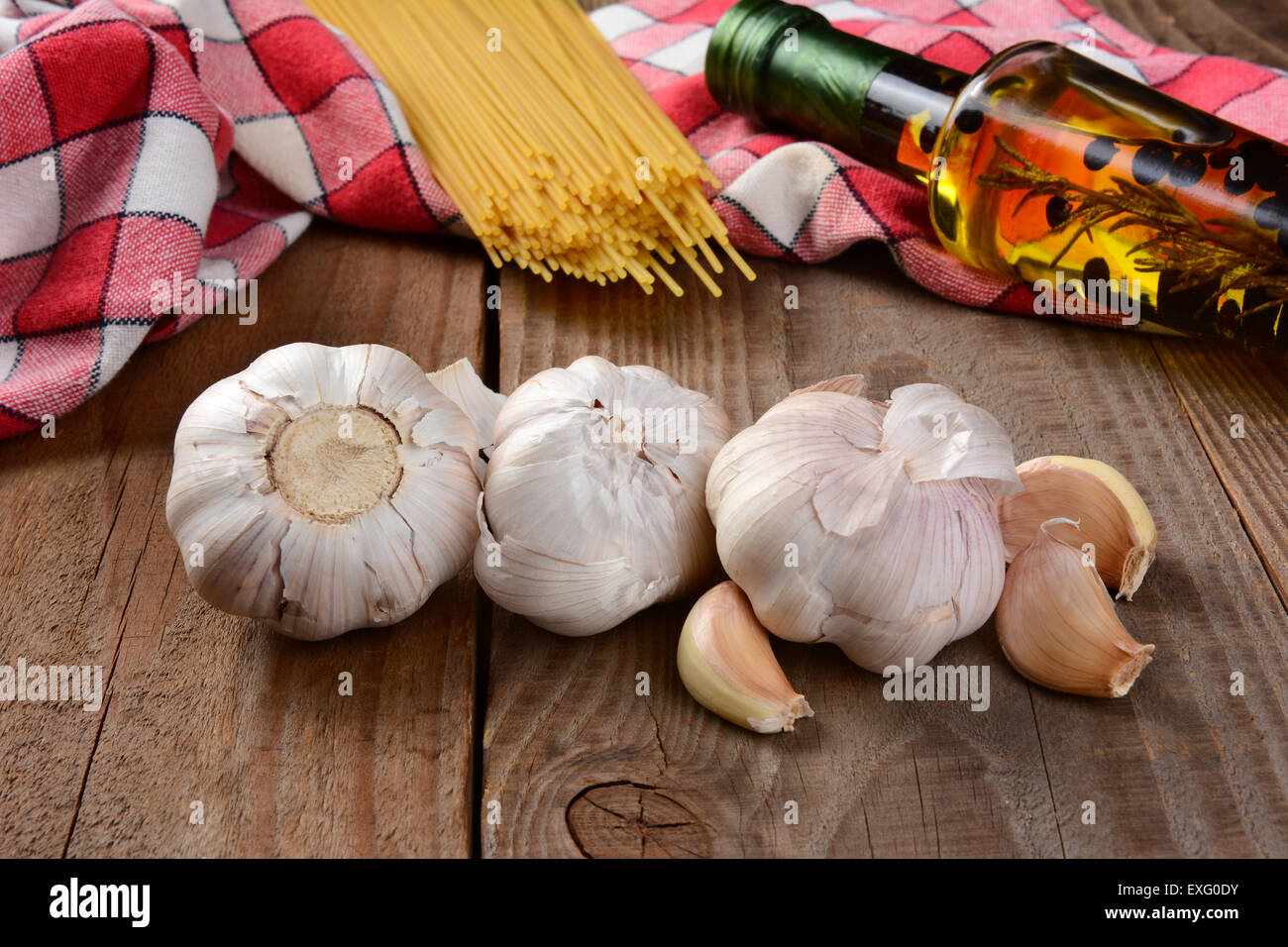 Italian cooking still life on a rustic wood table. Garlic cloves in the foreground with olive oil dried spaghetti and red and wh Stock Photo