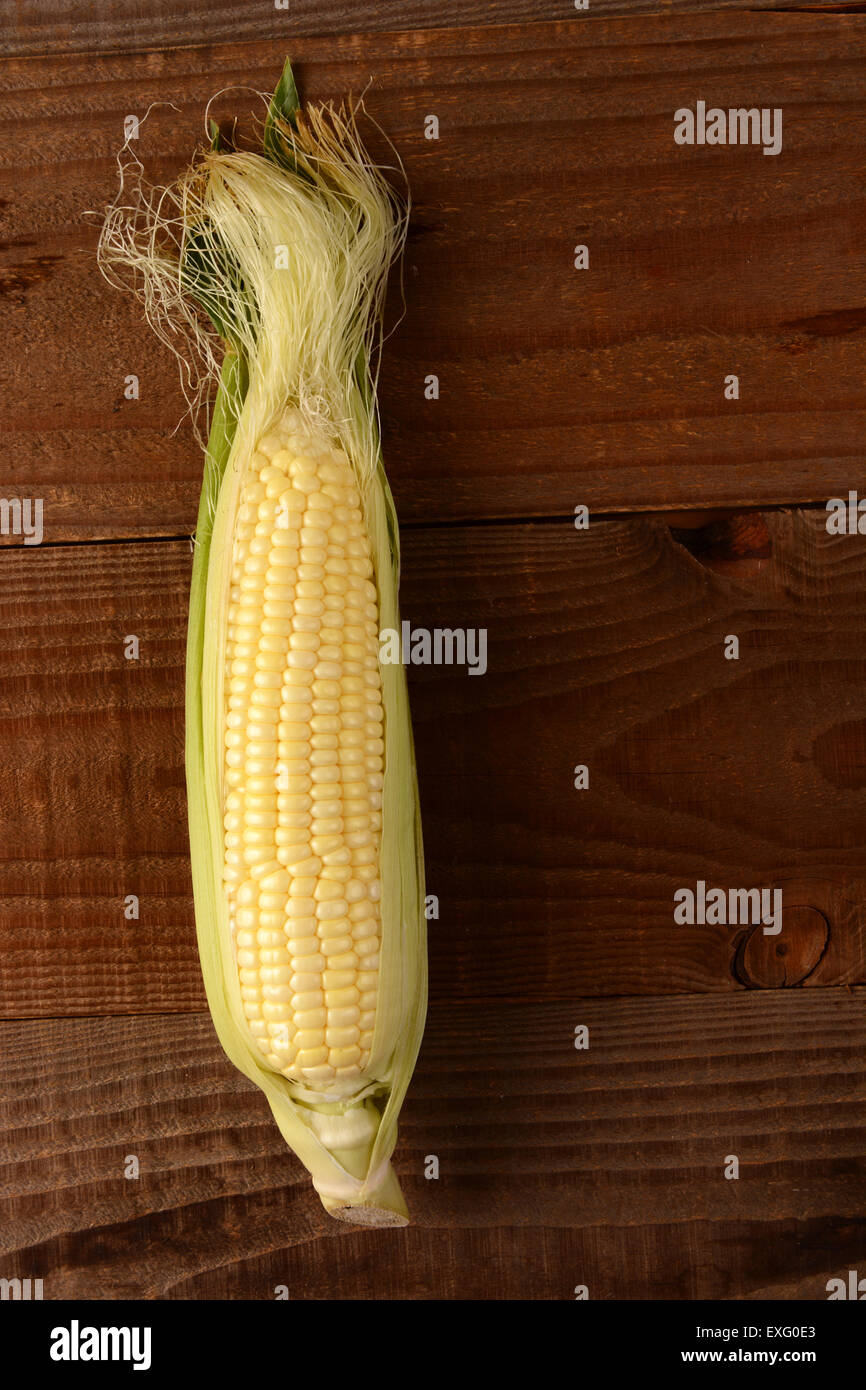 A single fresh picked and shucked ear of corn on the cob on a rustic wood table. The sweet corn is shot from a high angle Stock Photo