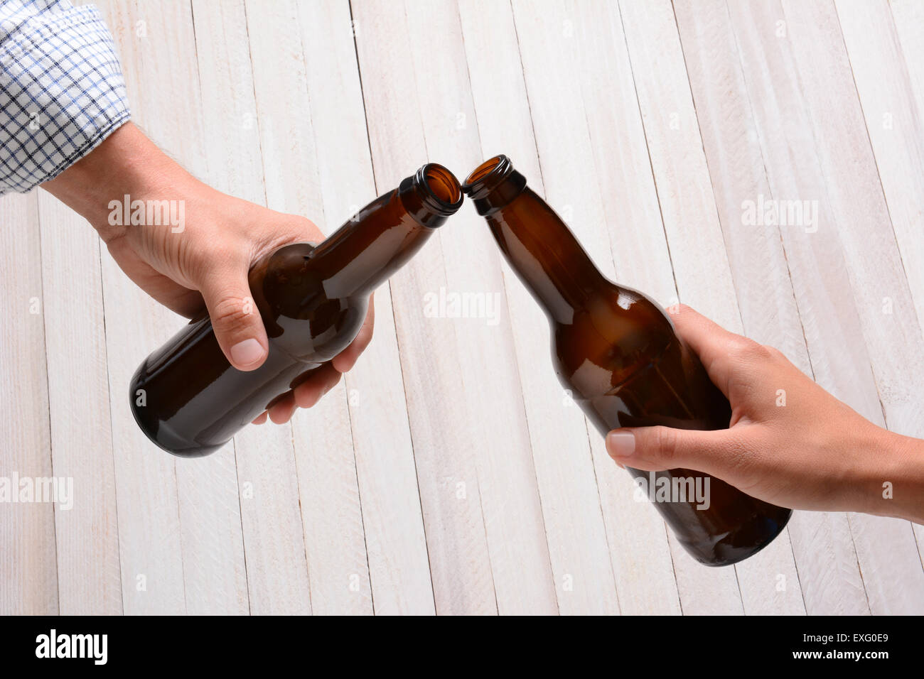 A man and a woman toasting with beer bottles. They are clinking the bottle tops over a rustic wood background. Stock Photo