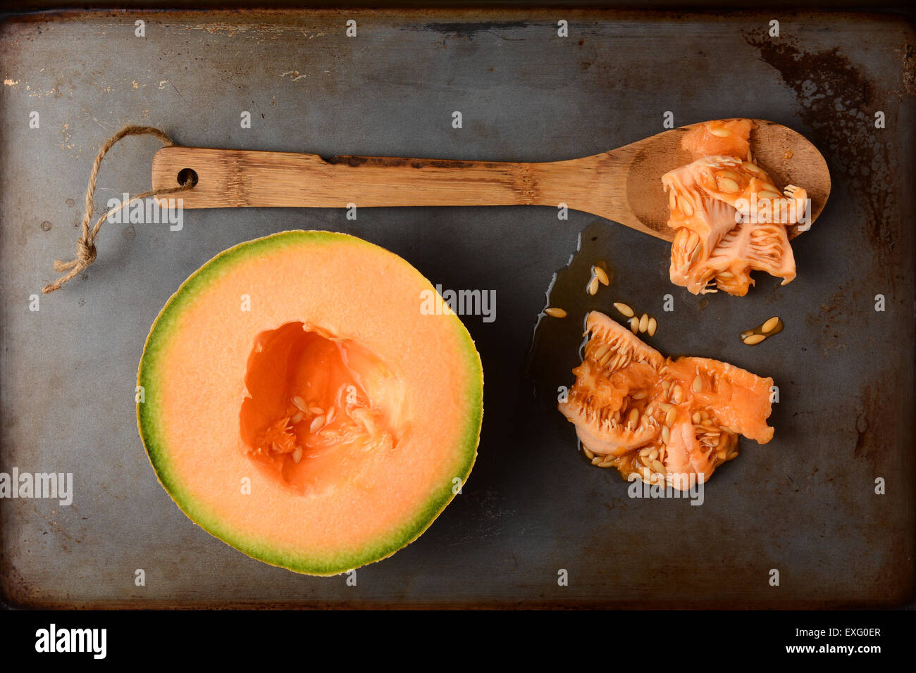 High angle shot of a cantaloupe half next to a wooden spoon and the seed pulp. Overhead view in vertical format on a used metal Stock Photo