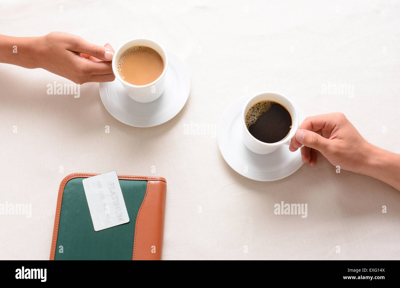 A man and woman reaching for their coffee cups across a cafe table. Overhead closeup with only the peoples hands being shown. Stock Photo