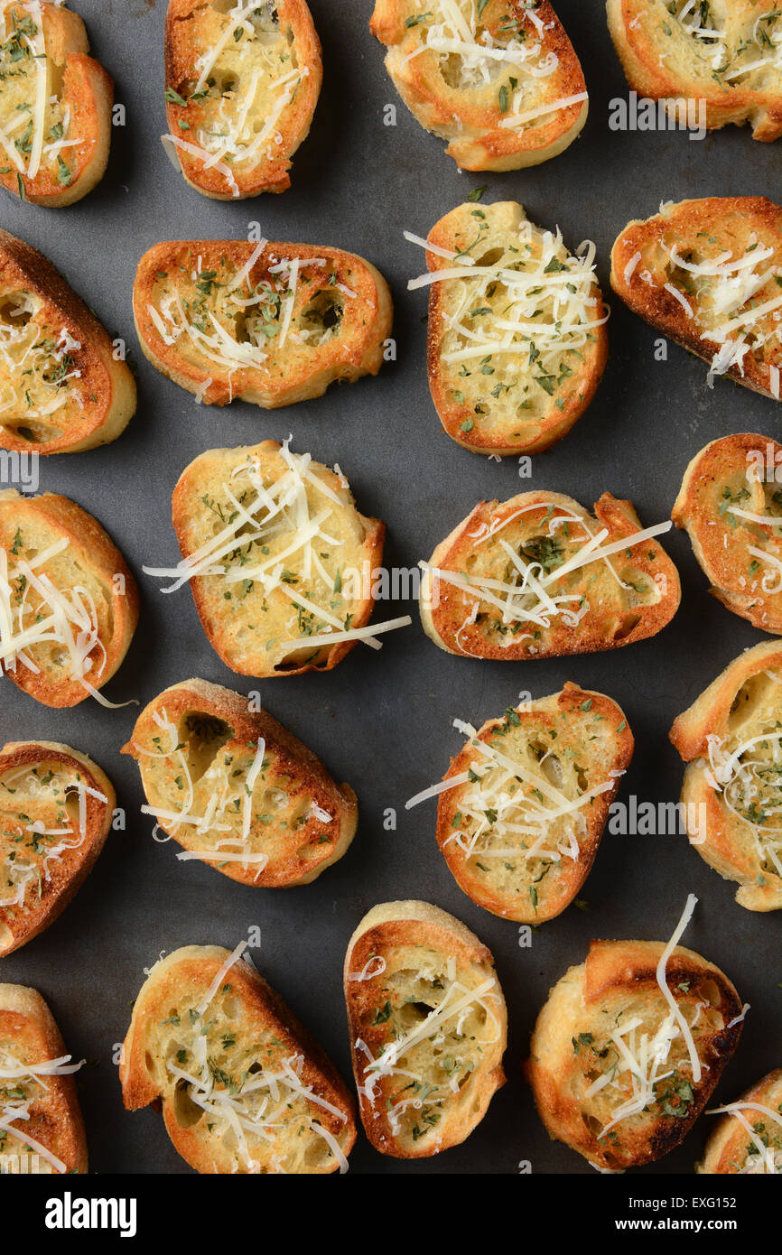 Closeup of a pan full of toasted garlic bread. The bread slices have parmesan cheese and other herbs and spices sprinkled on top Stock Photo