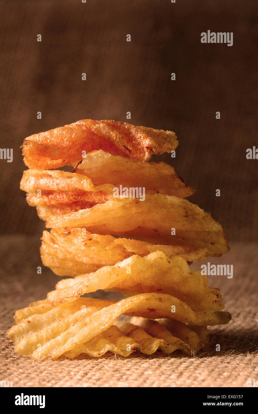 A stack of potato chips with warm side light. Vertical format on a burlap surface. Stock Photo