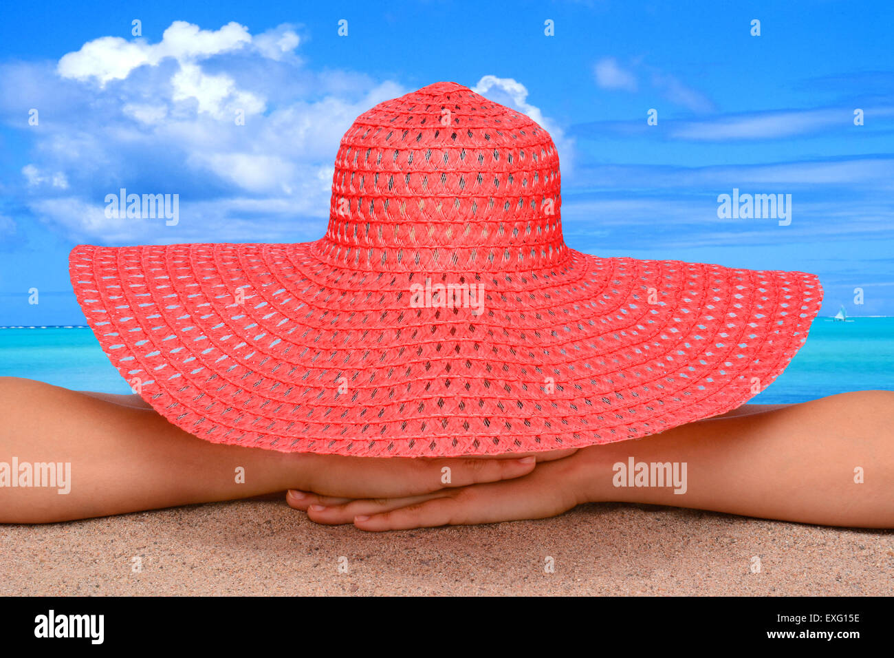 Closeup of a woman on the beach in a sun hat. The person is unrecognizable with a tropical ocean scenic in the background. Stock Photo