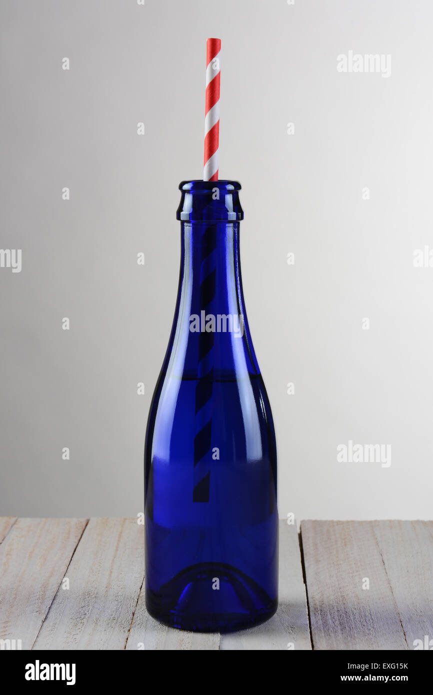 Closeup of a blue bottle with a red striped drinking straw. The bottle is on a rustic wood table with a light to dark gray backg Stock Photo