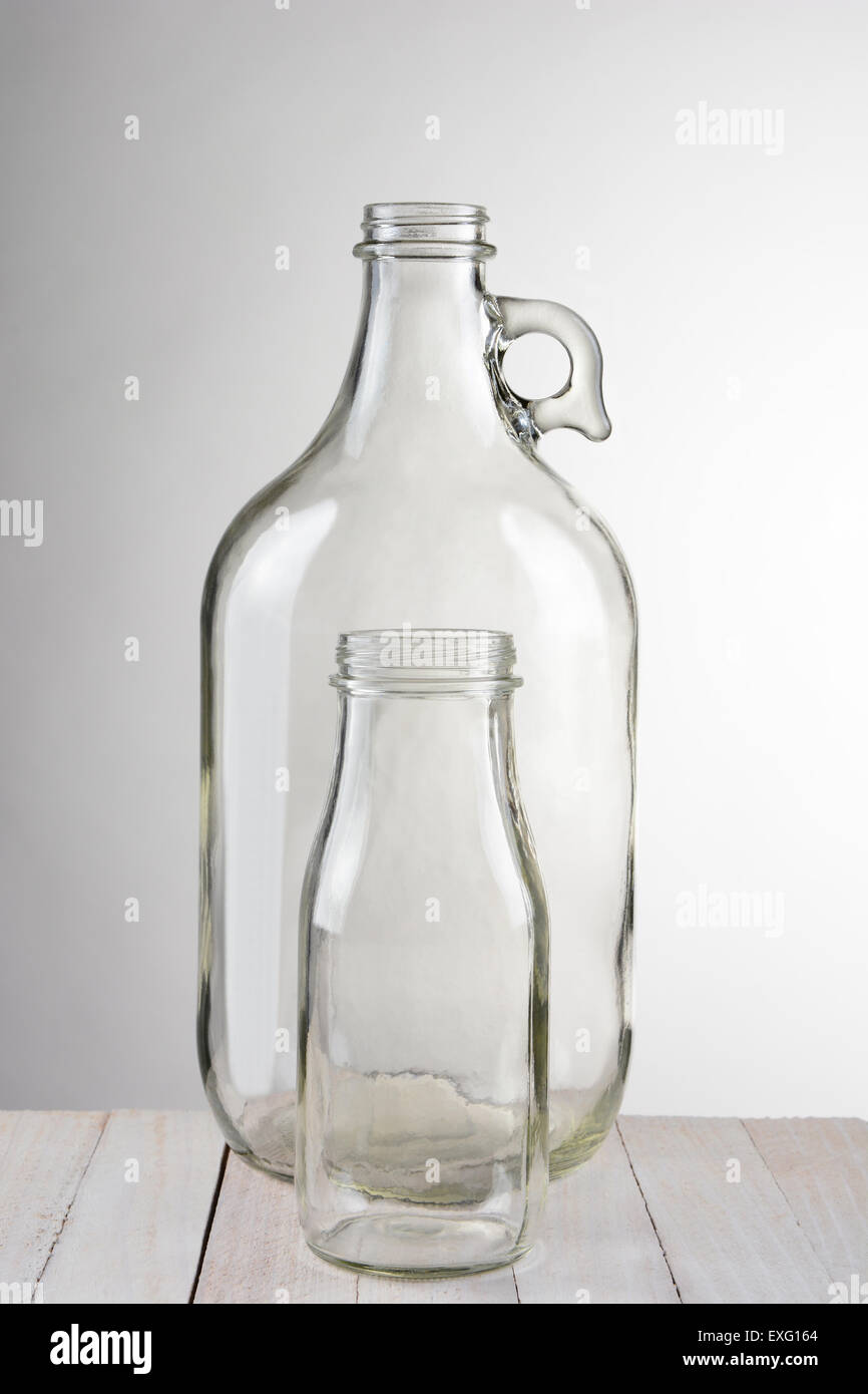 Two empty glass bottles, a small bottle in front of a larger container. Vertical format against a light to dark gray background. Stock Photo