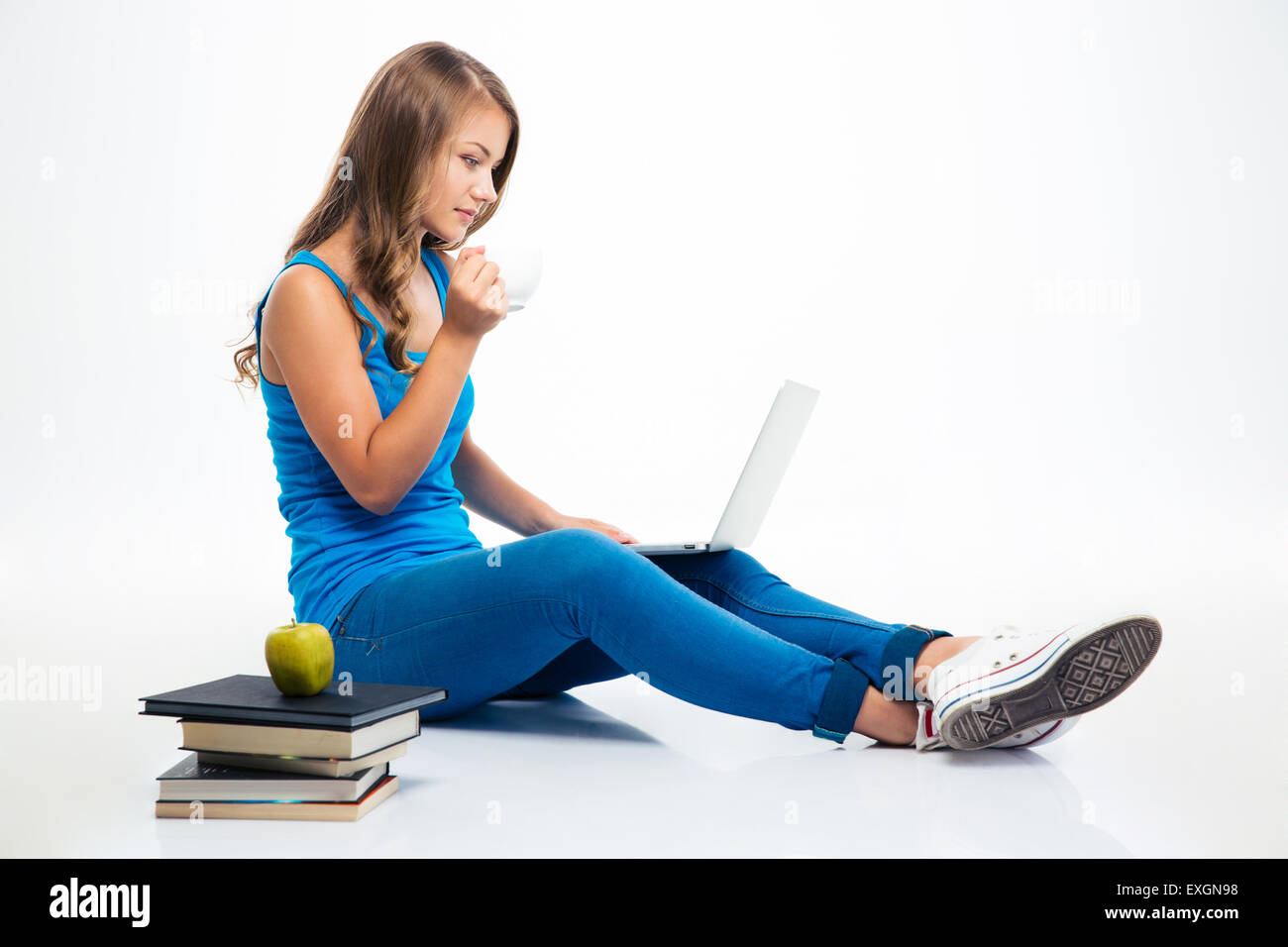 Young girl sitting on the floor with laptop and drinking coffee ...