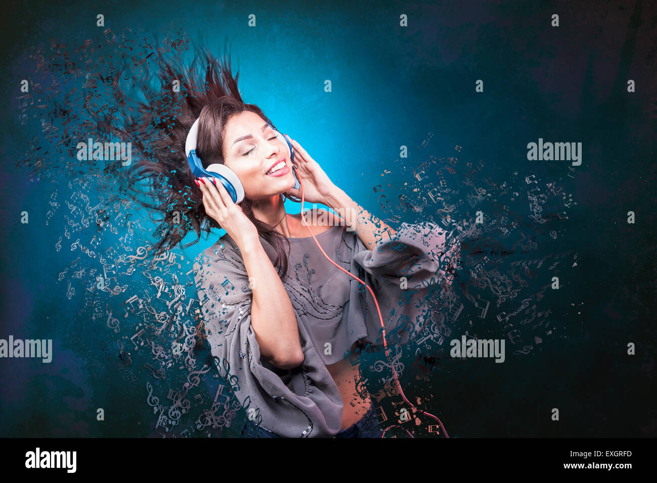 A young woman smiles, moves and wears headphones with flying notes. Stock Photo