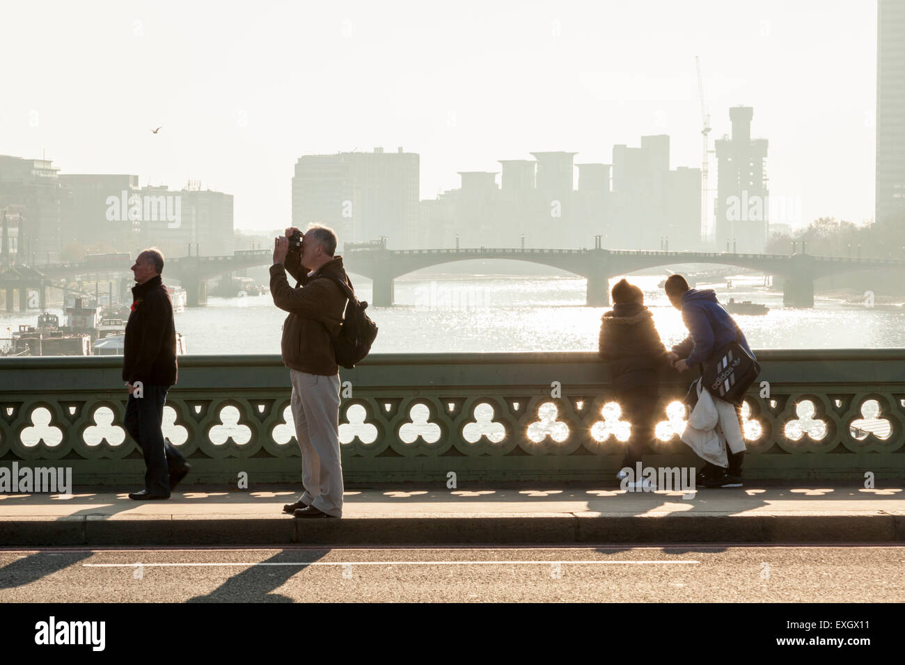 A person photographing, people looking at the river, and a man walking in winter sunlight, River Thames, Westminster Bridge, London, England, UK Stock Photo