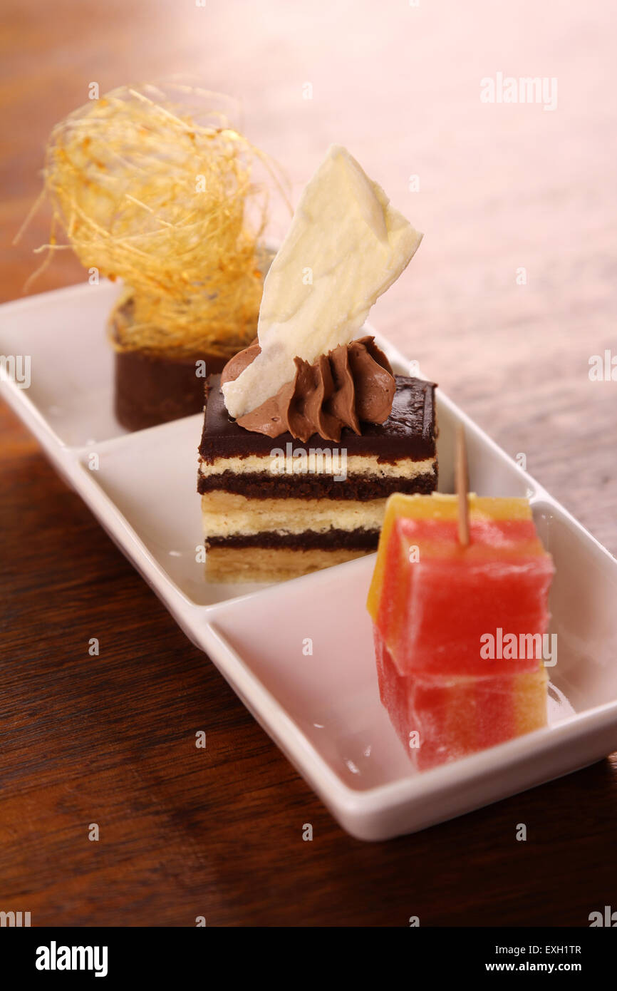 Three beautiful delicious gourmet desserts on a white plate. Chocolate layered cake, fudge, mousse and turkish delights. Stock Photo