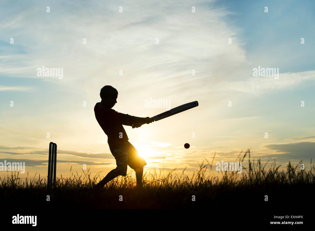 Silhouette of young boy playing cricket against a sunset background Stock Photo
