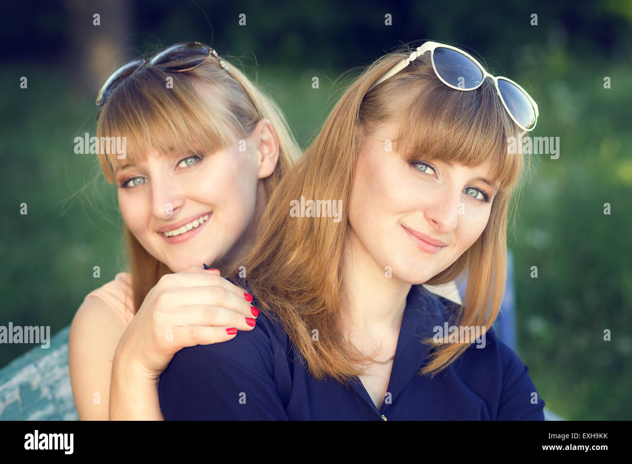 Portrait of twins sisters at the park. Two young beautiful girls looking straight. Warm color toned image Stock Photo