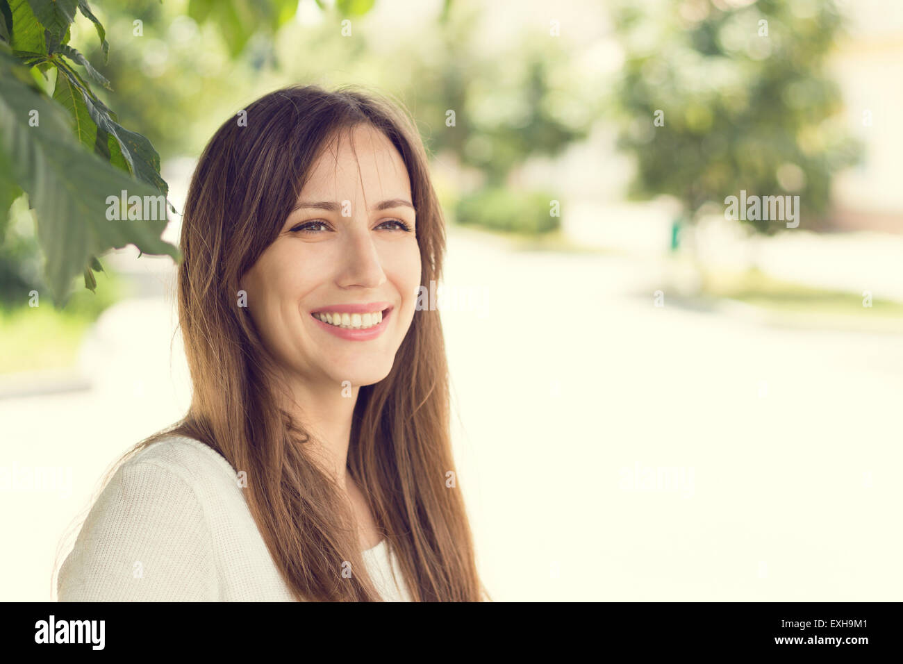 Young smiling woman with healthy teeth at sunny summer day. Pretty european girl with long hair. Warm color toned image Stock Photo
