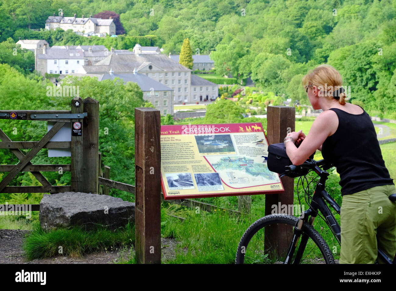 Female cyclist stopping at information board about Cressbrook Mill on the Monsal Trail cycle path in the Peak District, UK Stock Photo