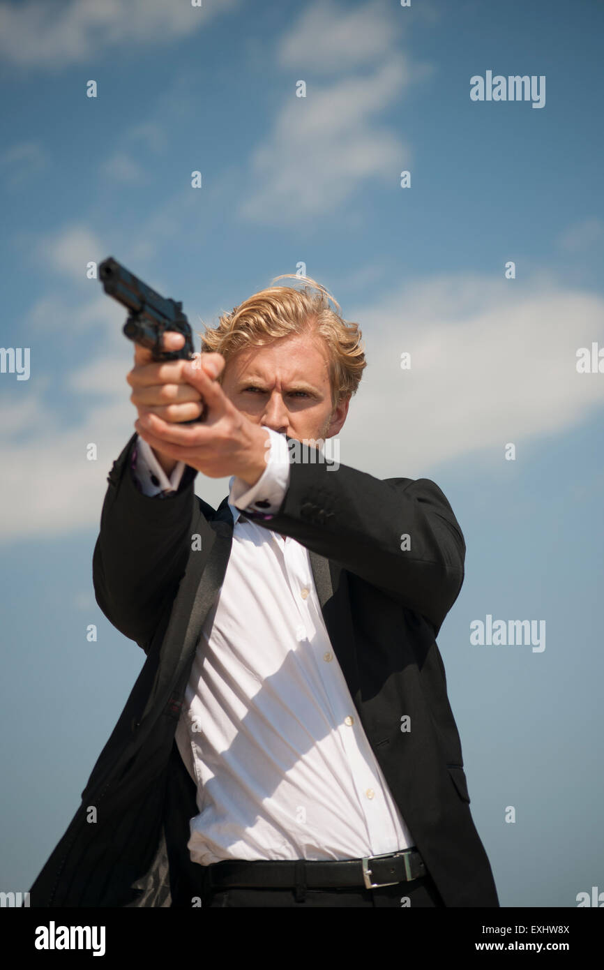 Man aiming a handgun, holding the gun with both hands wearing a black suit. Stock Photo
