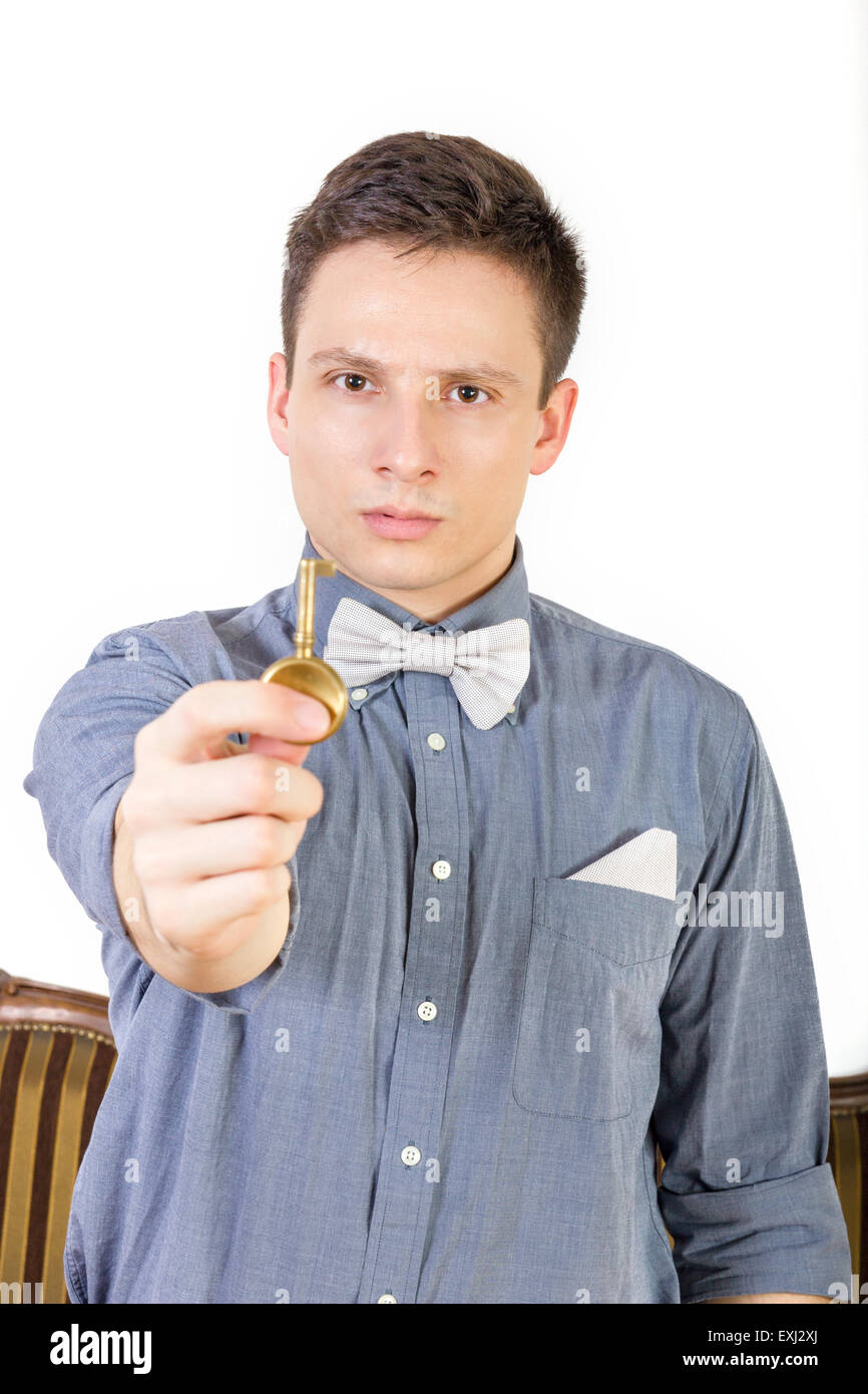 Man in a blue shirt with a bow tie holds the key. Male model shows a key to the door of copper or bronze at the camera. Young pe Stock Photo