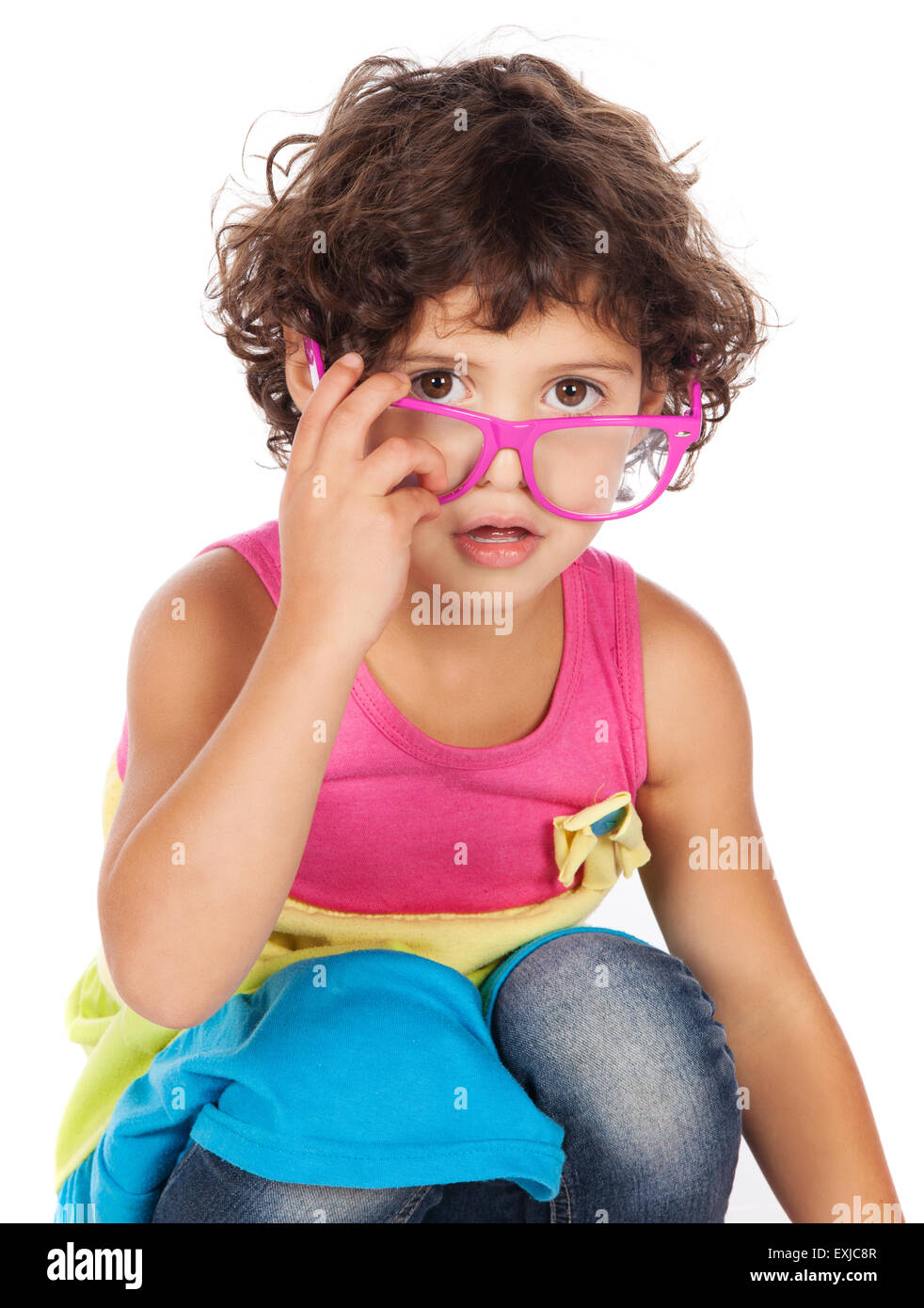 Adorable small caucasian child with curly hair wearing a pink blue and yellow dress. The girl is playing with funky sunglasses. Stock Photo