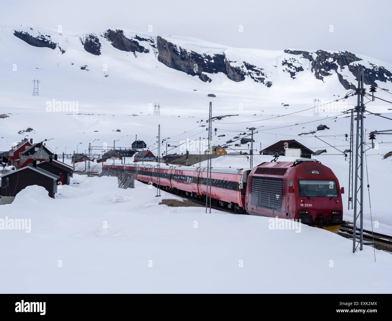Train passing Finse railway station, area covered with snow in late spring, highest railway station on railway Oslo-Bergen Stock Photo