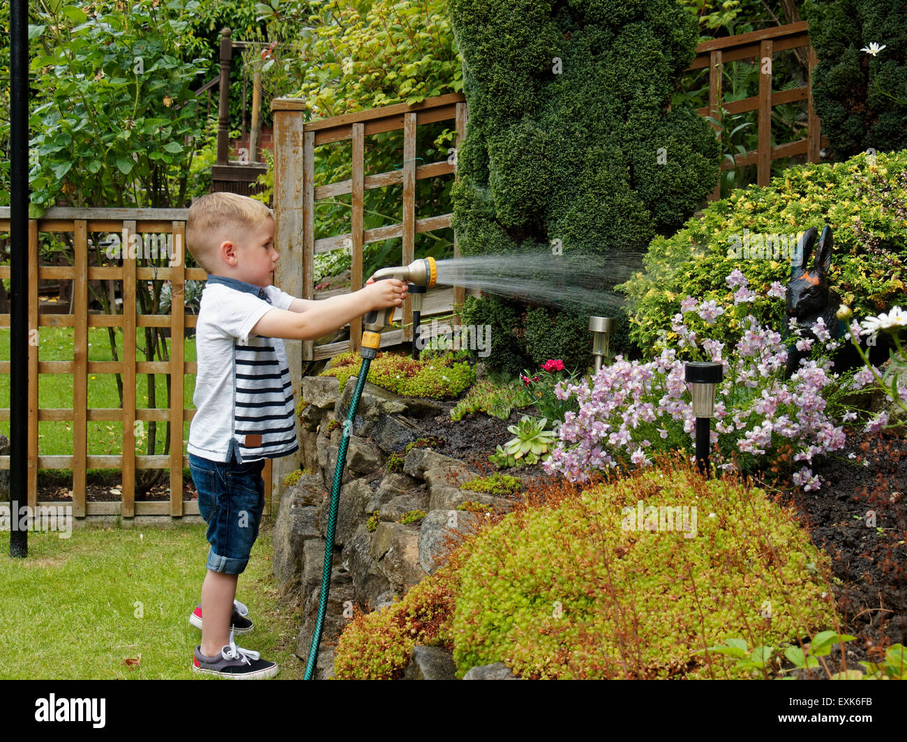Toddler with hose pipe watering garden plants Stock Photo