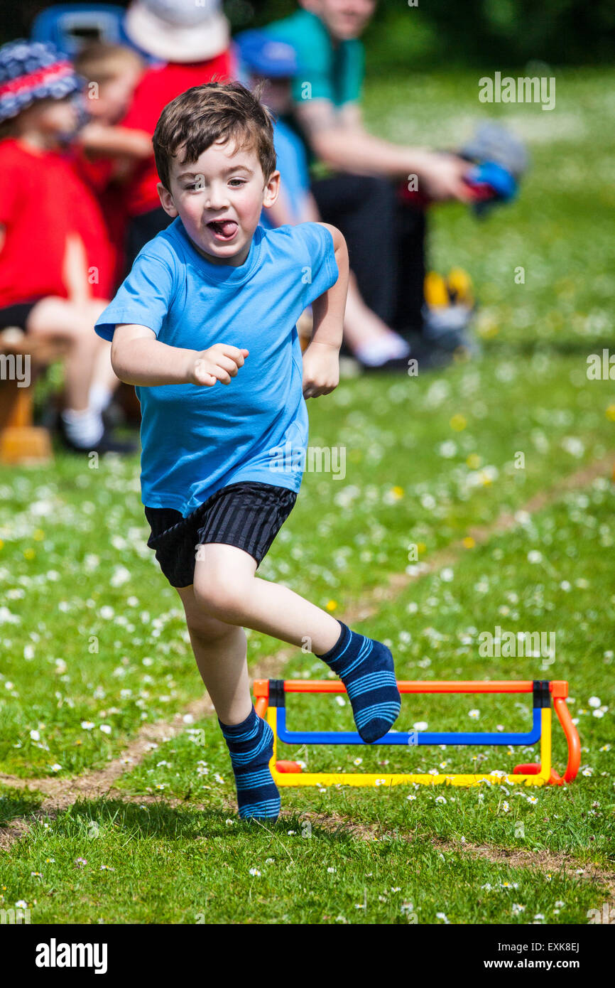 Young boy, 4, jumping over a hurdle in a pre-school sports day race Stock Photo