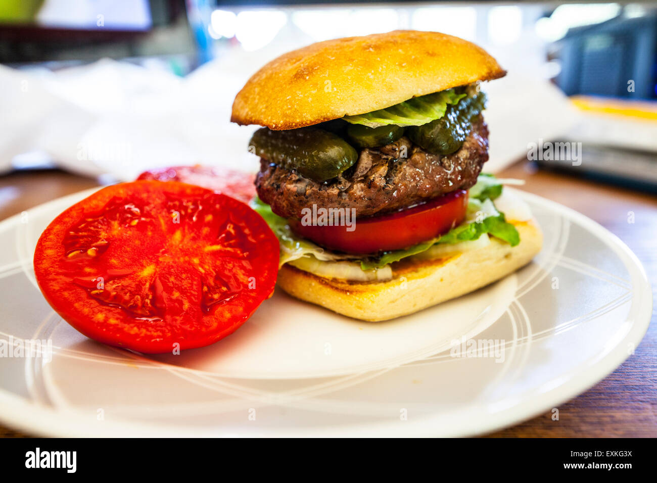 A Hamburger on a Torta roll with a fresh homegrown tomato from the garden with pickle and Romaine lettuce on a desk for lunch Stock Photo