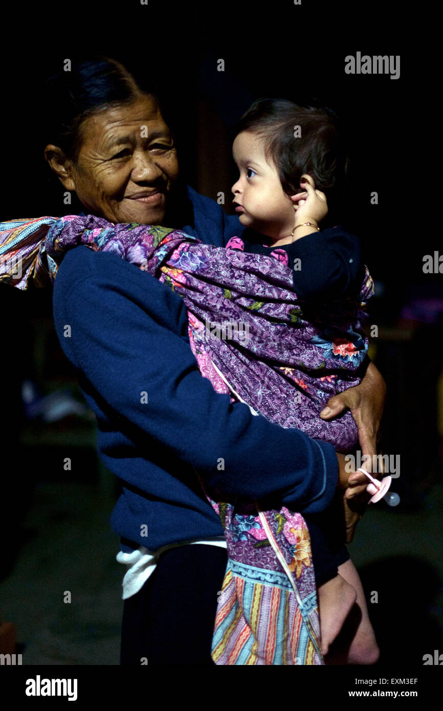 elderly lady acting as a nanny carrying baby girl in a sarong in the early hours of the morning in java indonesia Stock Photo