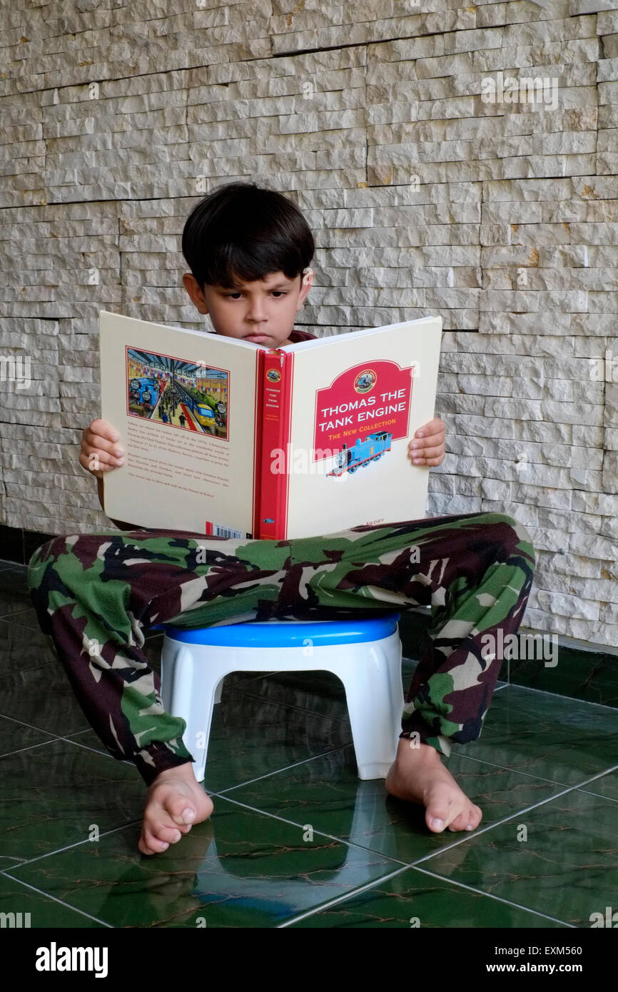 little boy learning to read his english thomas the tank engine book at home in java indonesia Stock Photo