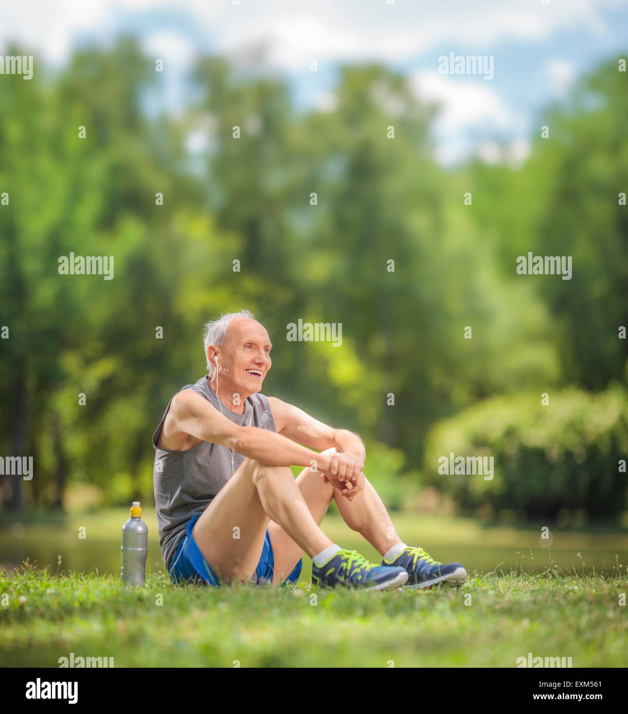 Athletic senior in sportswear sitting on grass in a park and listening to music on headphones shot with tilt and shift lens Stock Photo