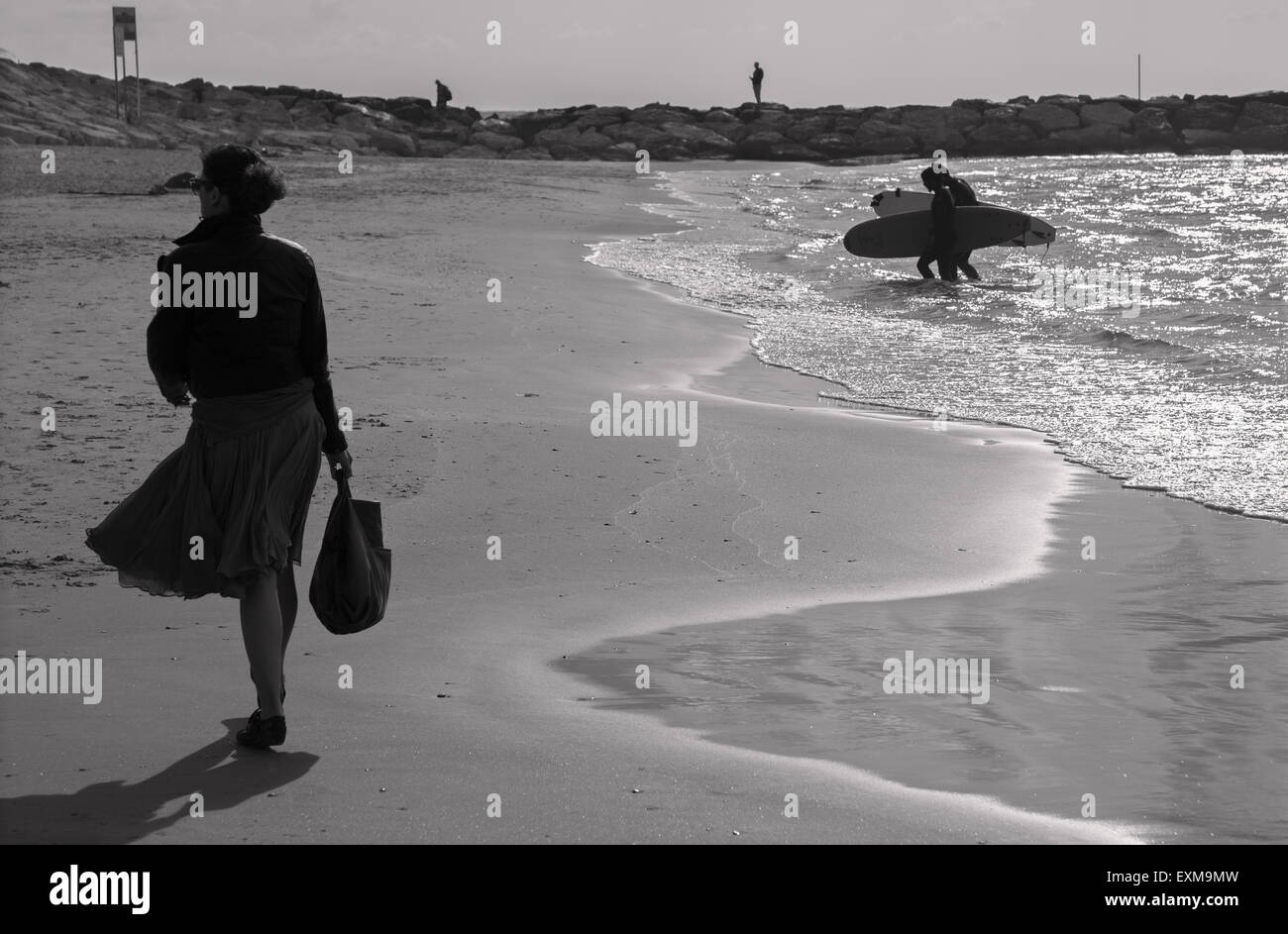 TEL AVIV, ISRAEL - MARCH 2, 2015: The silhouette of walked woman and surfers on the beach of Tel Aviv. Stock Photo