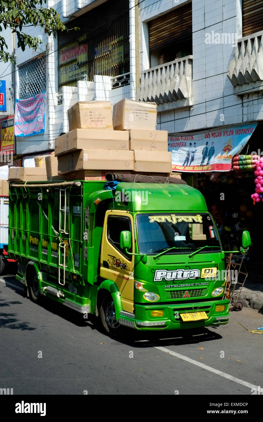 workers unload boxes from a dangerously overladen lorry as they deliver goods to a shop in solo java indonesia Stock Photo