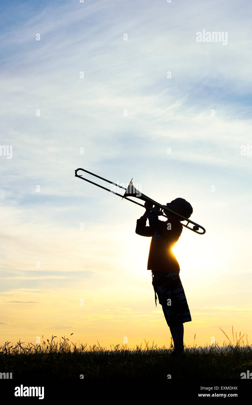 Silhouette of young boy playing a trombone against a sunset background Stock Photo