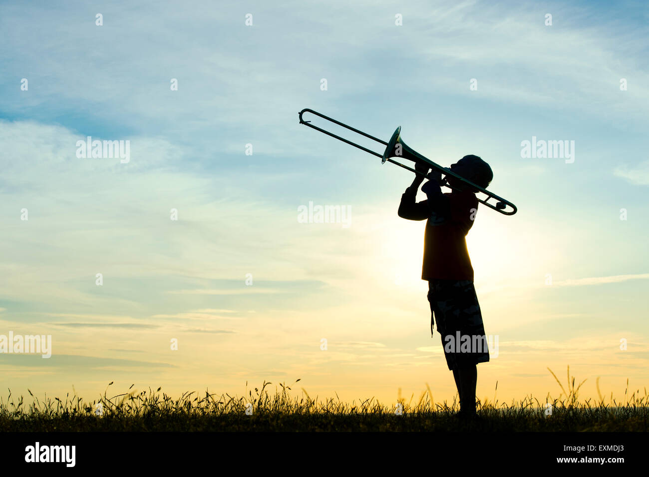 Silhouette of young boy playing a trombone against a sunset background Stock Photo