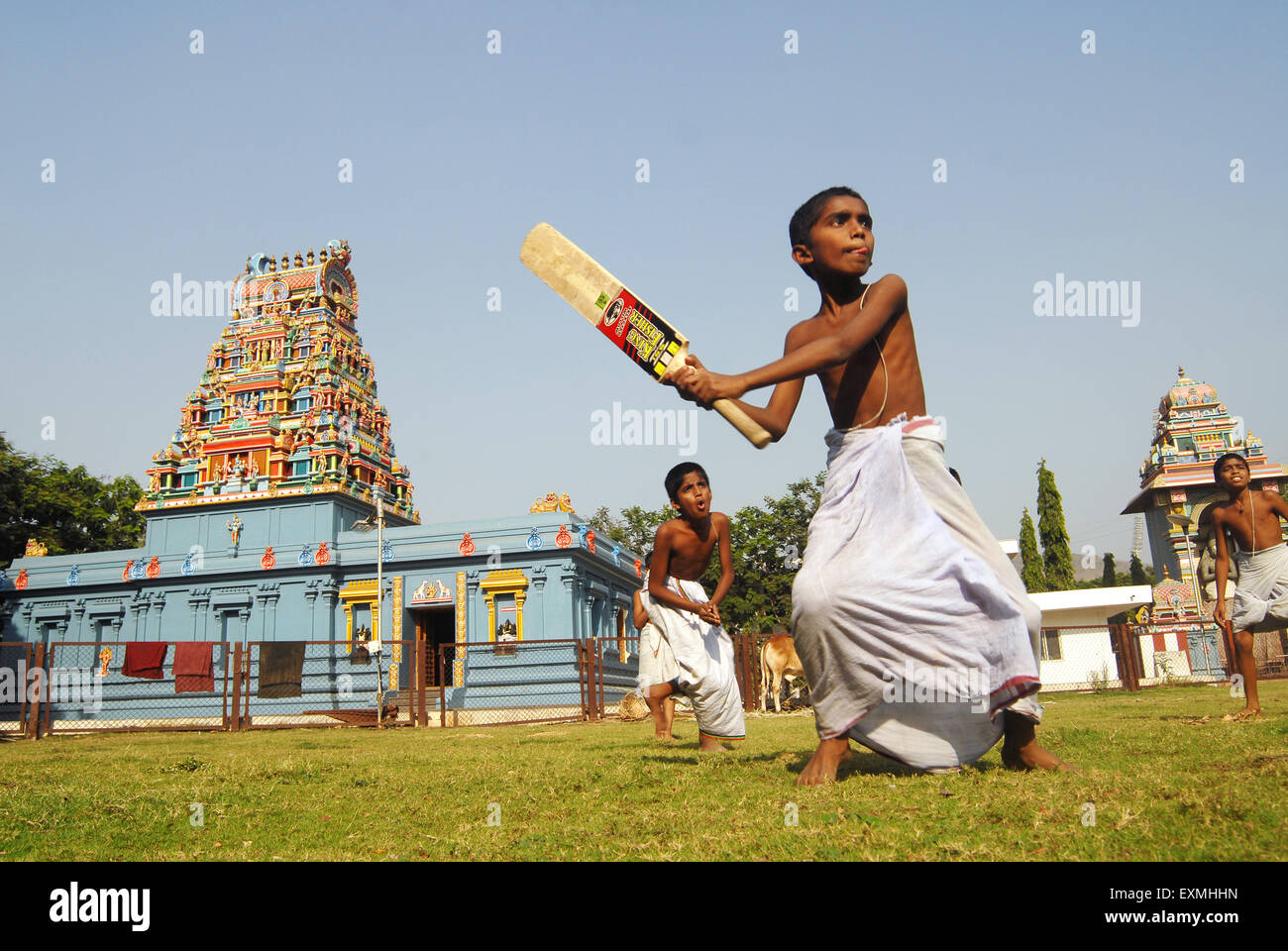 Boys wearing white lungis playing game of cricket in front of temple at Navi Mumbai , New Bombay , Maharashtra , India Stock Photo