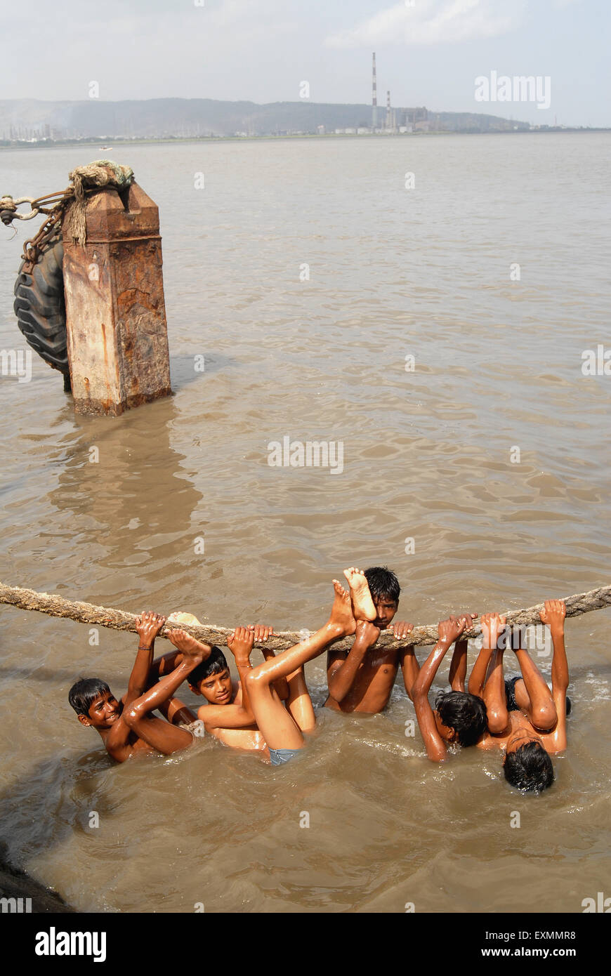 Children enjoy a dip hanging over thick rope to beat summer heat at Sewri creek in Bombay Mumbai ; Maharashtra ; India Stock Photo