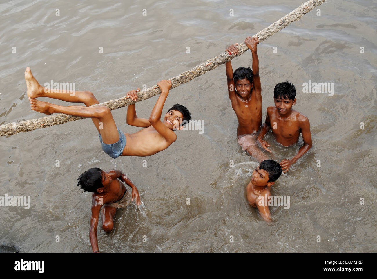Children enjoy dip hanging over thick rope to beat summer heat at Sewri creek in Bombay Mumbai ; Maharashtra ; India Stock Photo