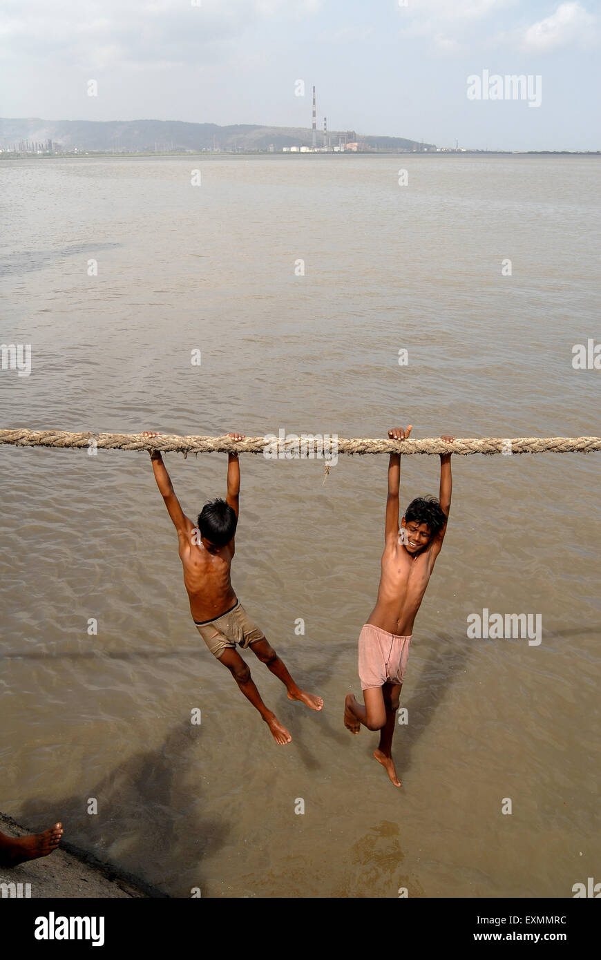 Children enjoy a dip hanging over a thick rope to beat the summer heat at Sewri creek in Bombay Mumbai ; Maharashtra ; India Stock Photo
